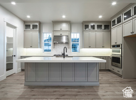 Kitchen featuring a center island with sink, gray cabinetry, double oven, and extractor fan