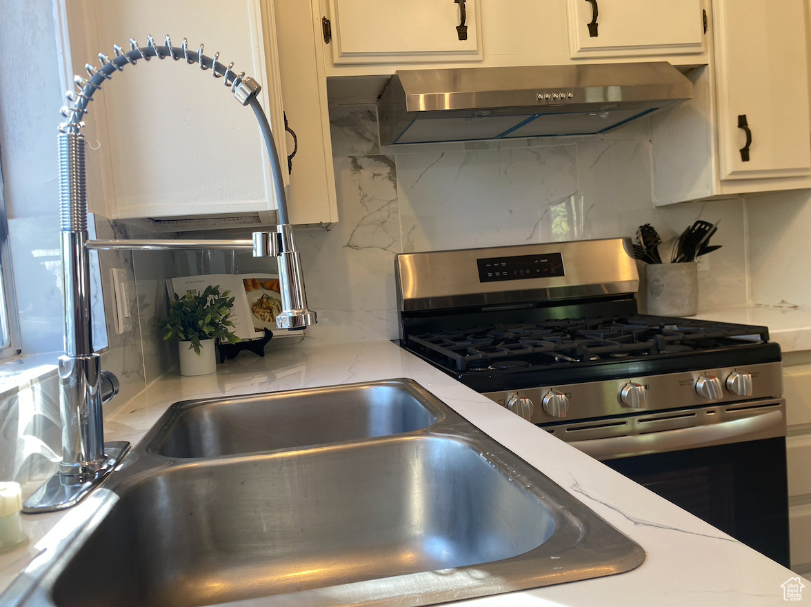 Kitchen featuring stainless steel range with gas stovetop, backsplash, white cabinetry, and range hood