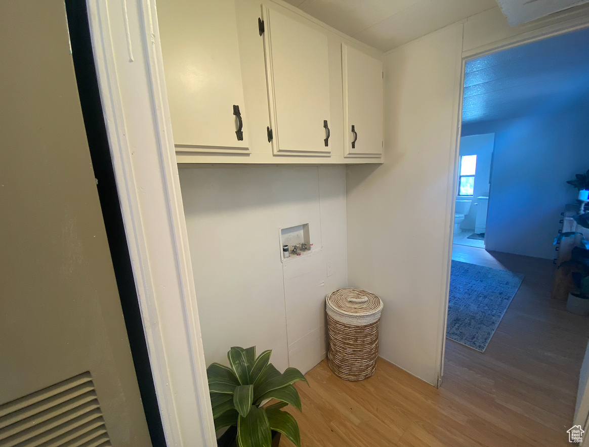 Clothes washing area with cabinets, hookup for a washing machine, and light hardwood / wood-style flooring