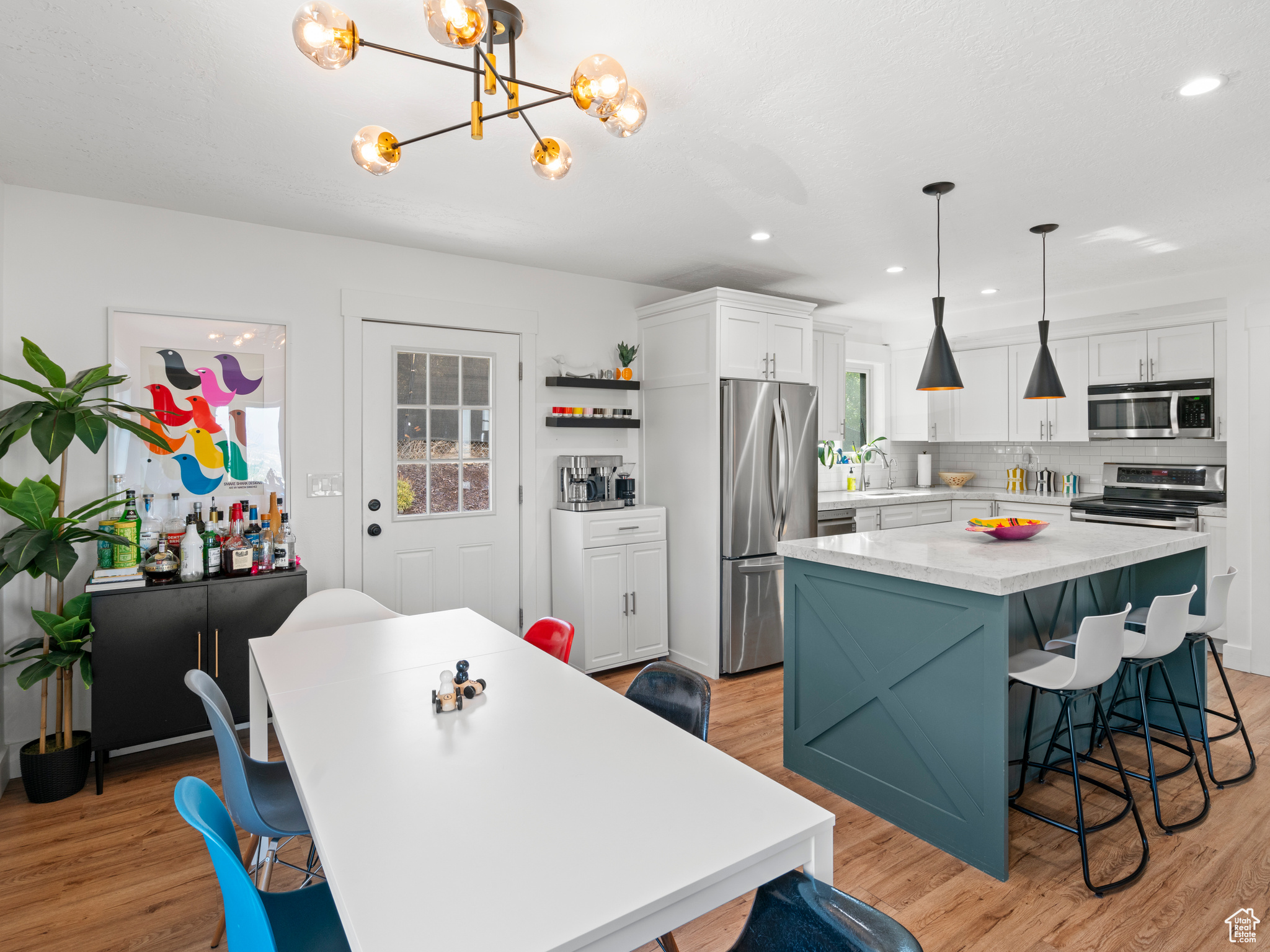 Kitchen with appliances with stainless steel finishes, decorative light fixtures, a kitchen island, and light hardwood / wood-style floors