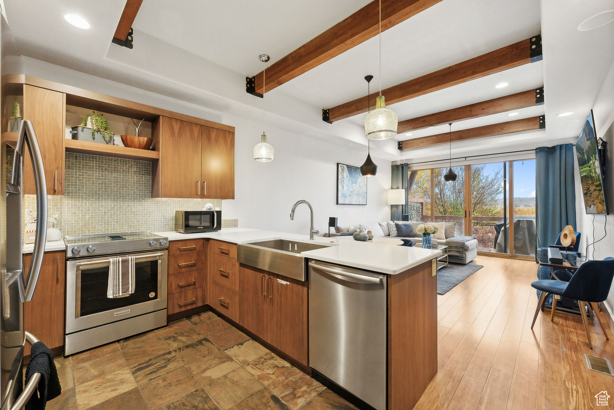 Kitchen with kitchen peninsula, appliances with stainless steel finishes, beamed ceiling, pendant lighting, and sink