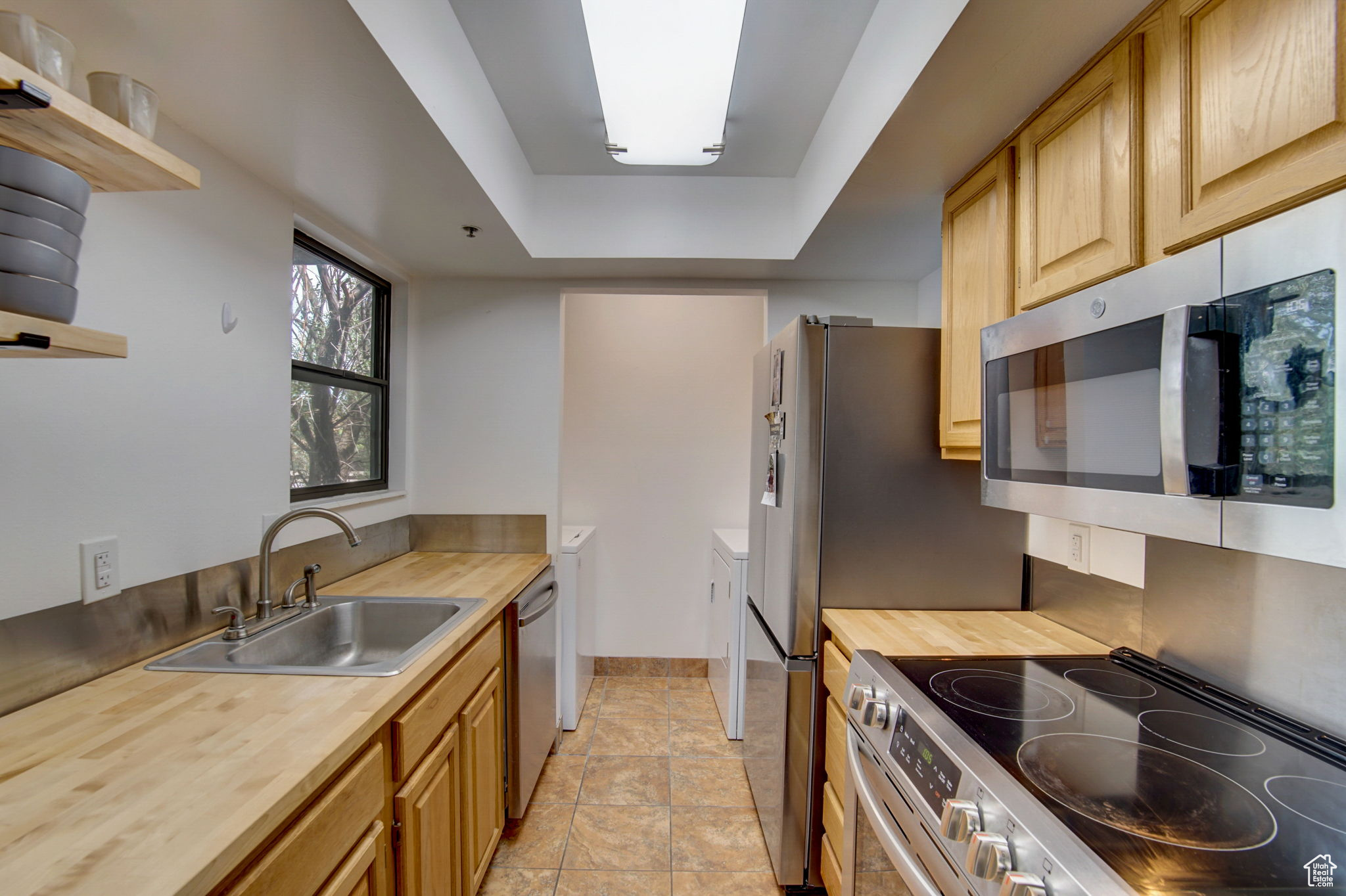 Kitchen featuring light brown cabinets, sink, a tray ceiling, appliances with stainless steel finishes, and butcher block counters