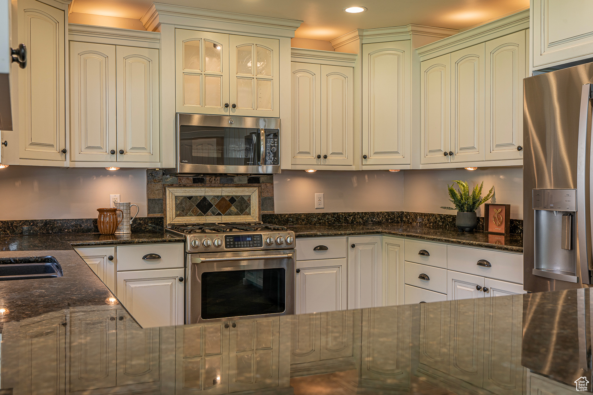 Kitchen with appliances with stainless steel finishes, white cabinetry, and dark stone counters