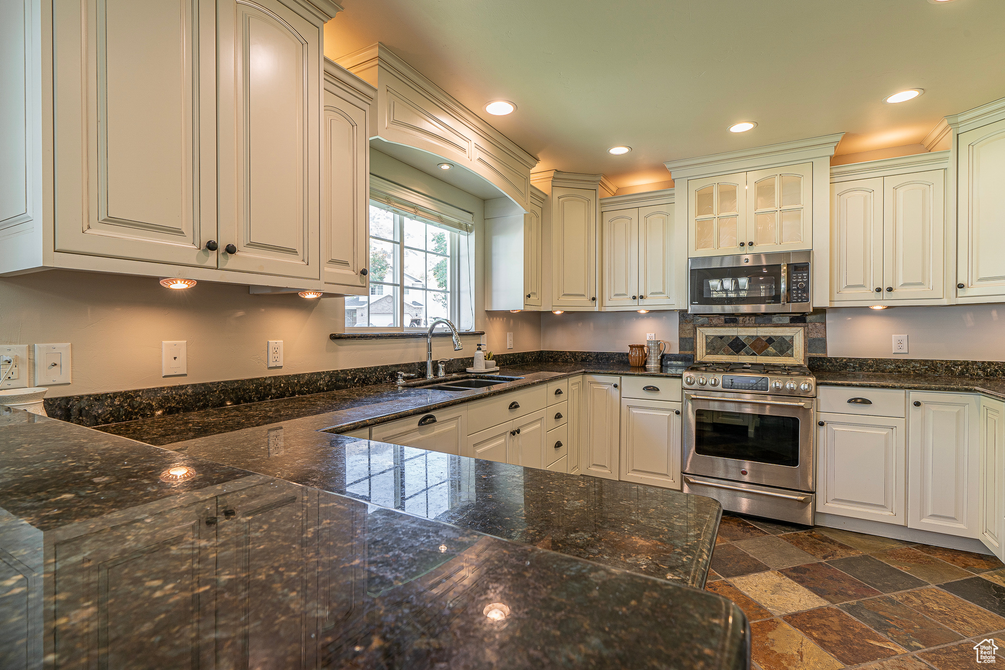 Kitchen with sink, white cabinetry, stainless steel appliances, and dark stone counters