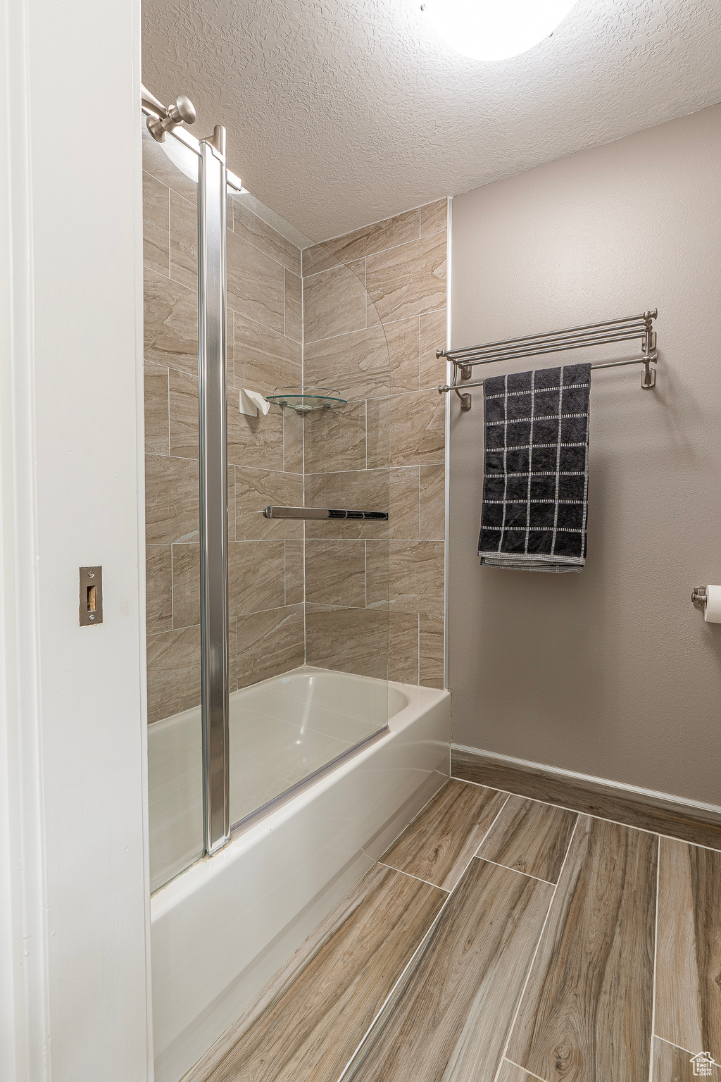 Bathroom with wood-type flooring, a textured ceiling, and tiled shower / bath