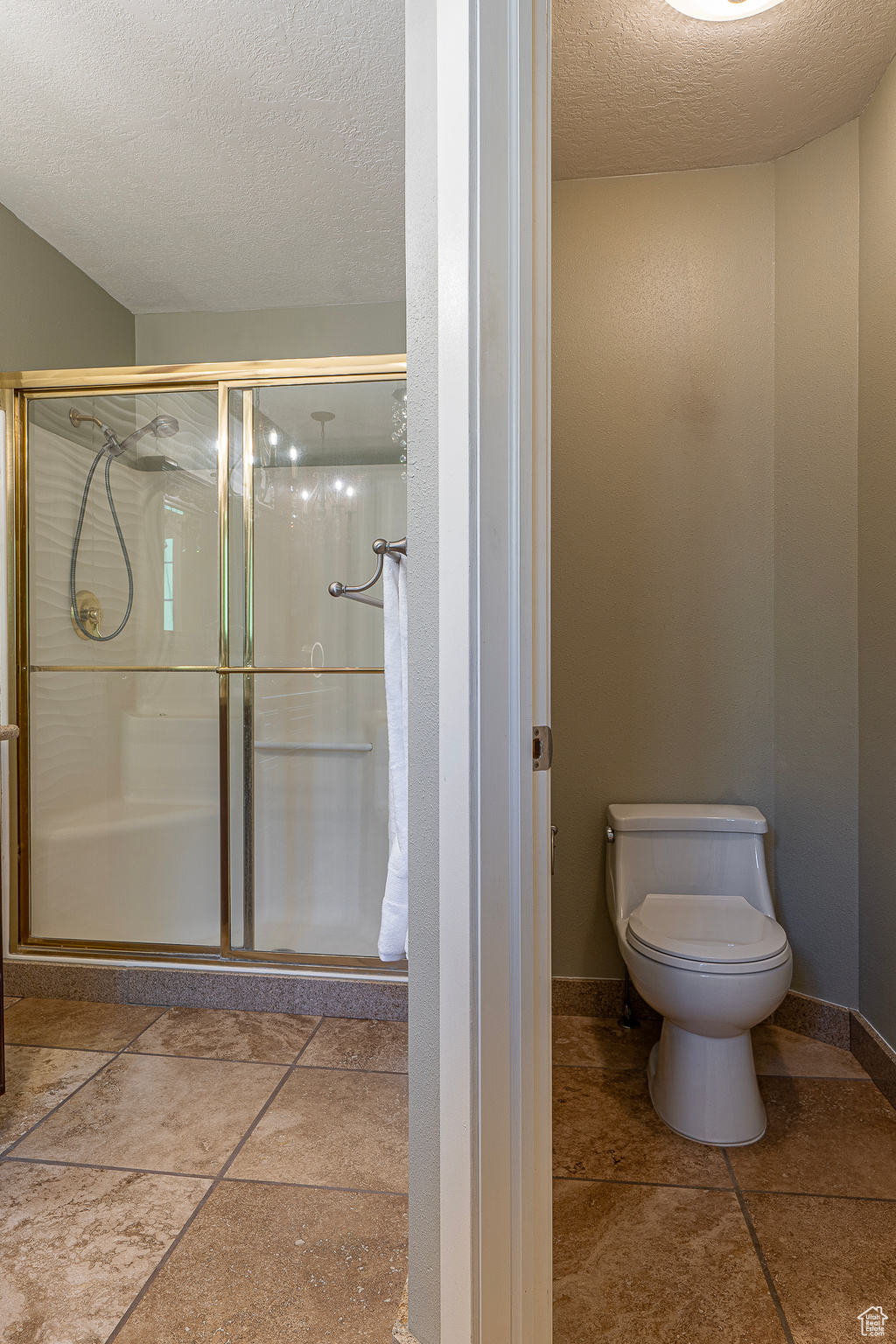 Bathroom featuring toilet, a textured ceiling, and a shower with shower door