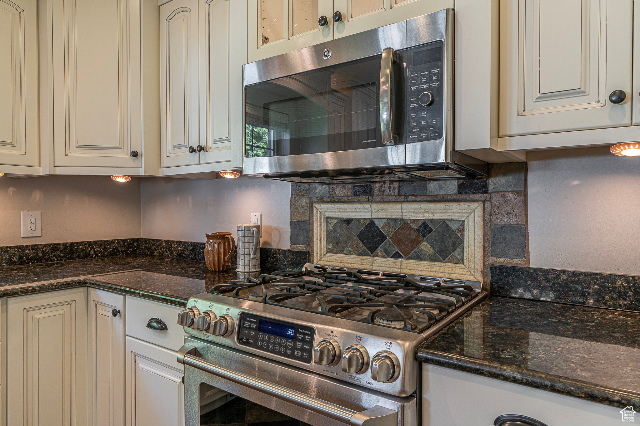 Kitchen with appliances with stainless steel finishes, dark stone countertops, and backsplash