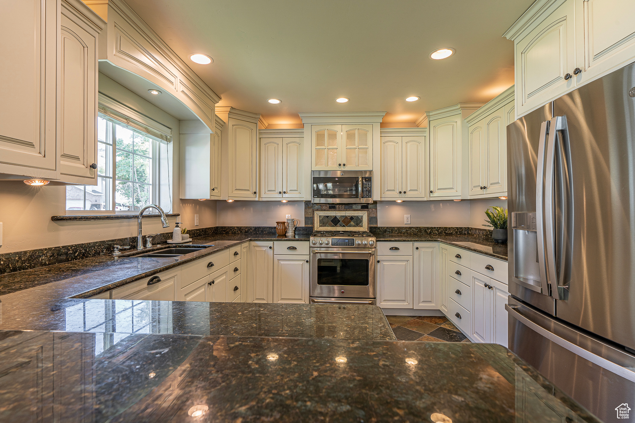 Kitchen featuring sink, appliances with stainless steel finishes, white cabinets, and dark stone countertops