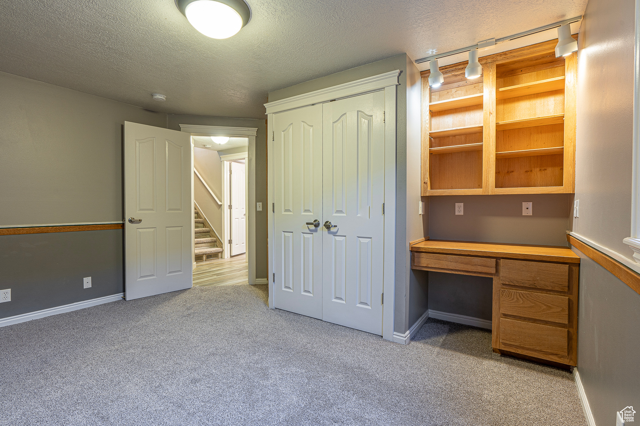 Unfurnished office featuring light colored carpet, a textured ceiling, and built in desk