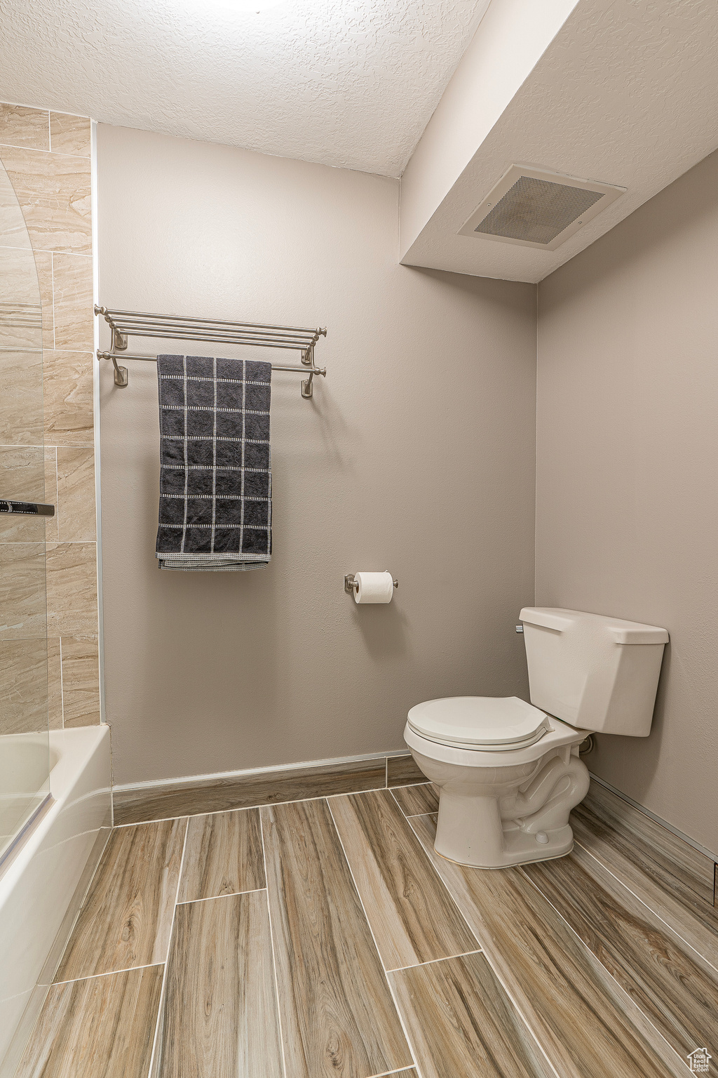 Bathroom with shower / washtub combination, a textured ceiling, and toilet