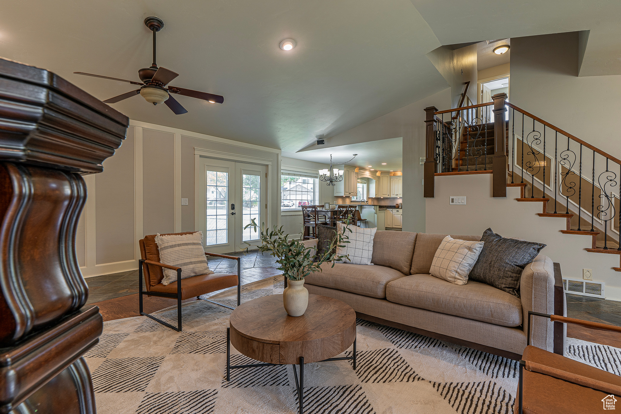 Living room with lofted ceiling, french doors, and ceiling fan with notable chandelier