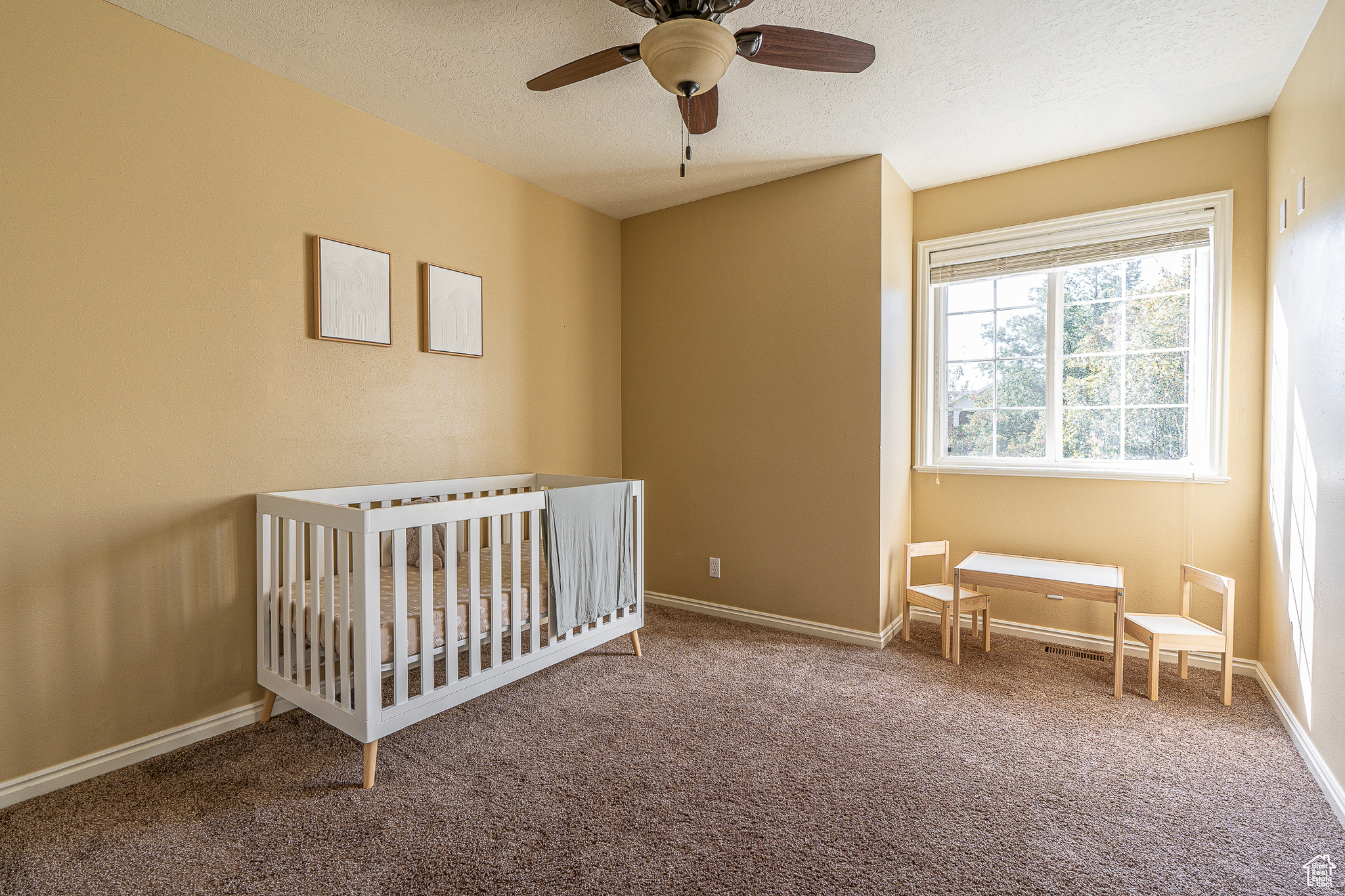 Unfurnished bedroom featuring ceiling fan, carpet, a textured ceiling, and a nursery area