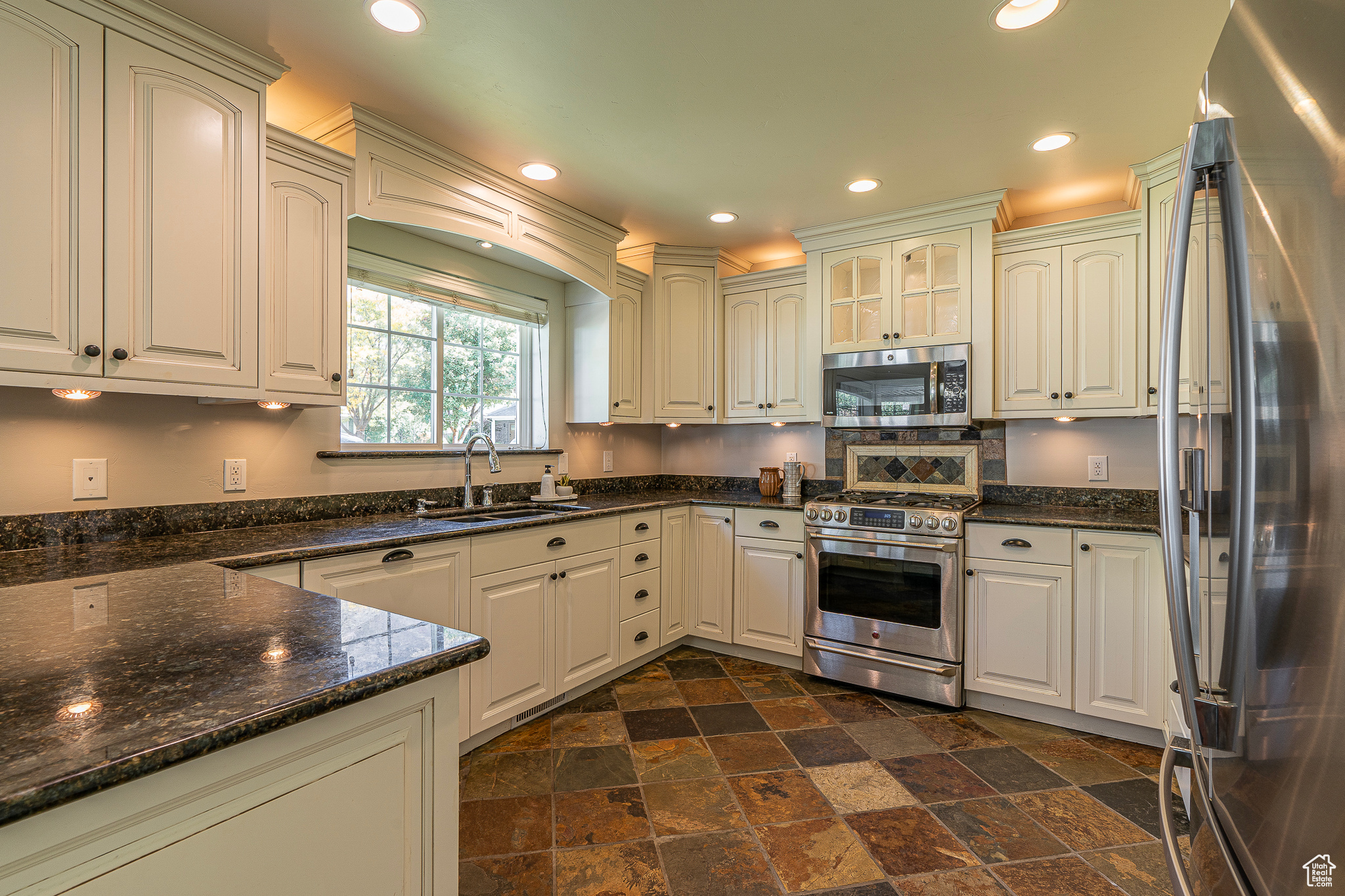 Kitchen featuring sink, white cabinetry, stainless steel appliances, and dark stone counters