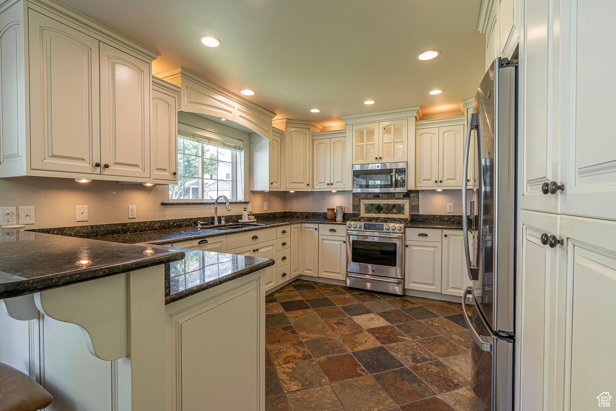 Kitchen featuring sink, appliances with stainless steel finishes, kitchen peninsula, and dark stone counters