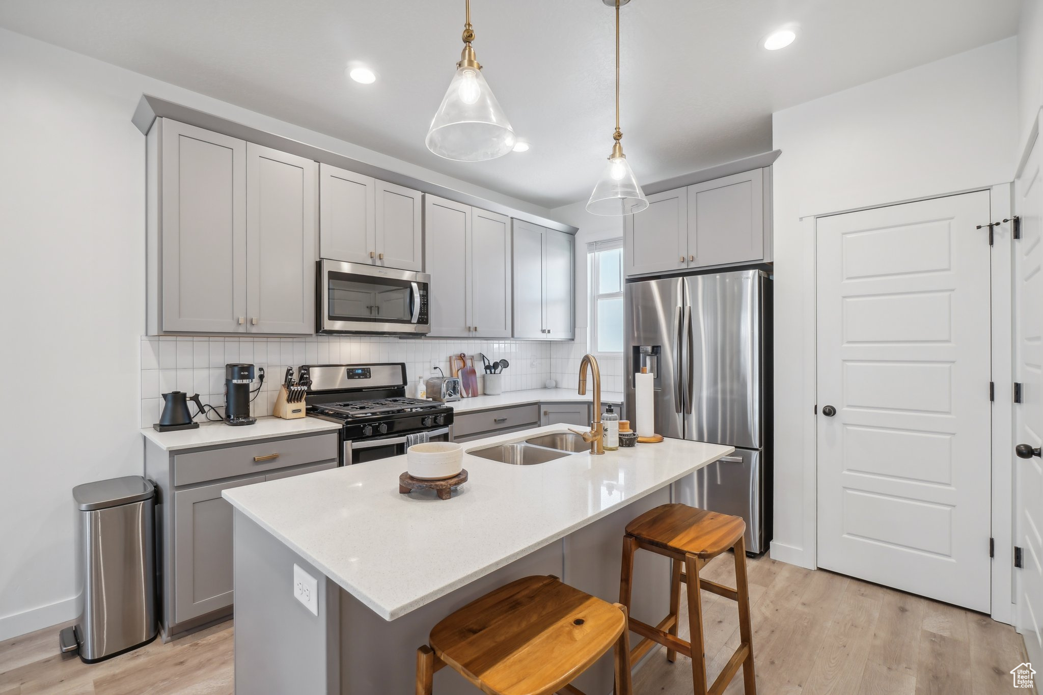 Kitchen featuring appliances with stainless steel finishes, light hardwood / wood-style flooring, a center island with sink, and hanging light fixtures