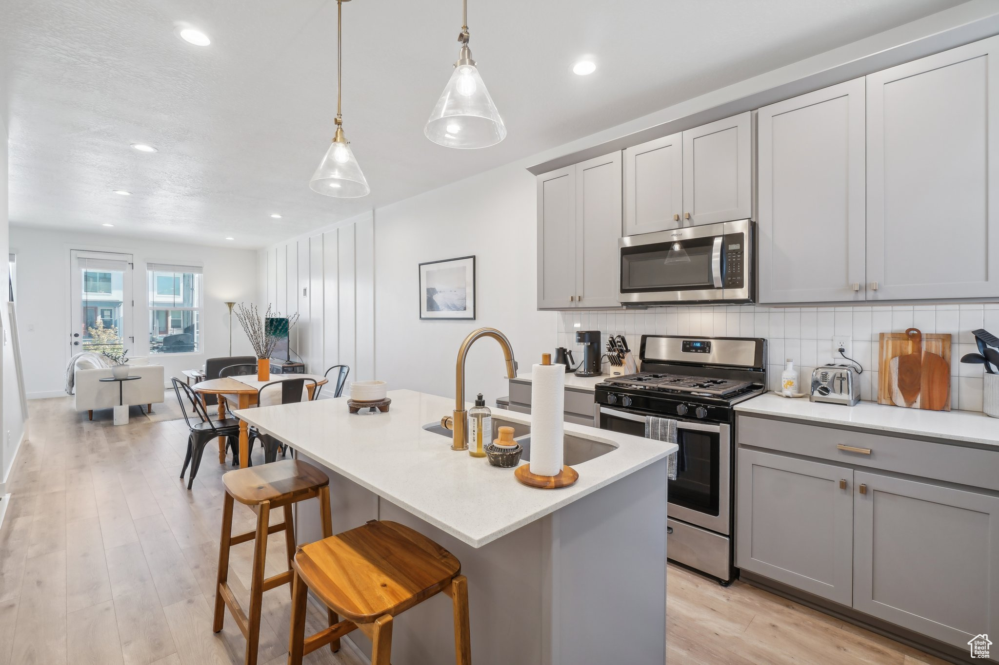 Kitchen with a center island with sink, appliances with stainless steel finishes, pendant lighting, light hardwood / wood-style floors, and gray cabinetry