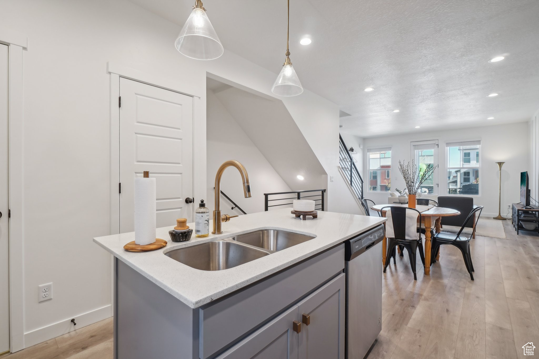 Kitchen featuring sink, dishwasher, an island with sink, decorative light fixtures, and gray cabinets