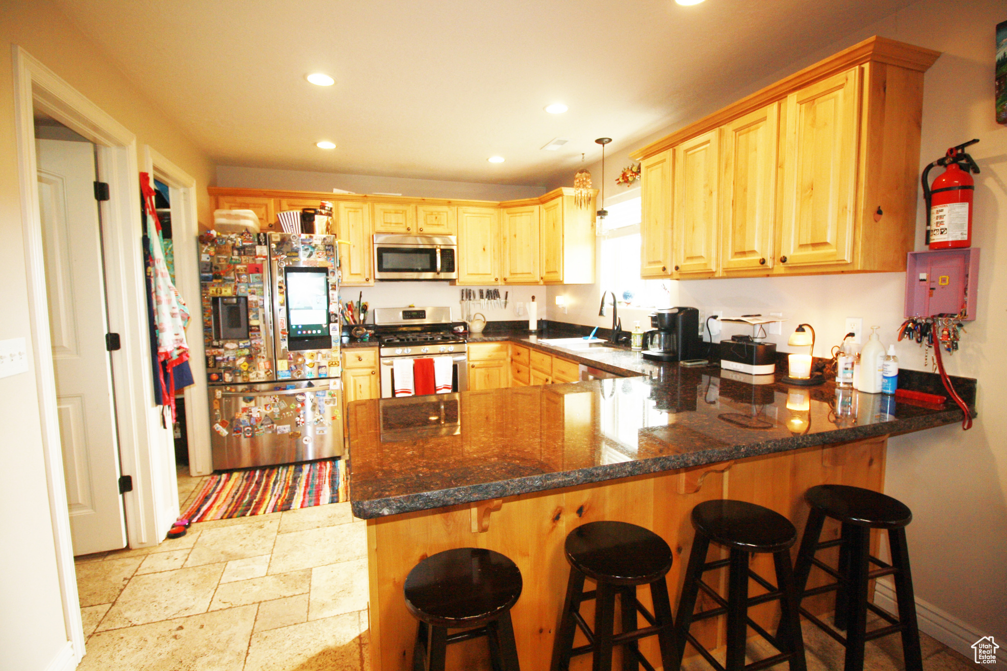 Kitchen with appliances with stainless steel finishes, sink, kitchen peninsula, dark granite counters, and decorative light fixtures