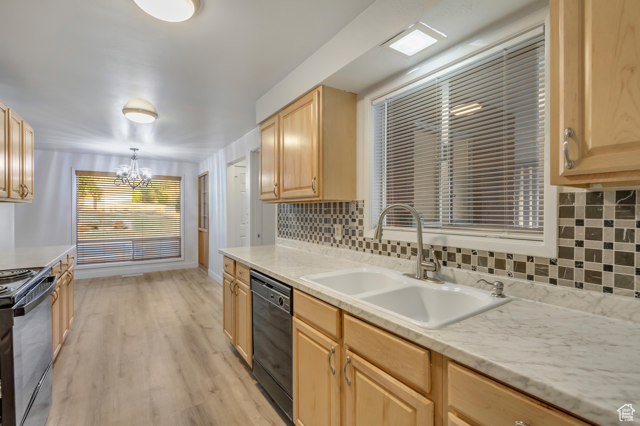 Kitchen with black dishwasher, light brown cabinetry, light wood-type flooring, pendant lighting, and stainless steel range