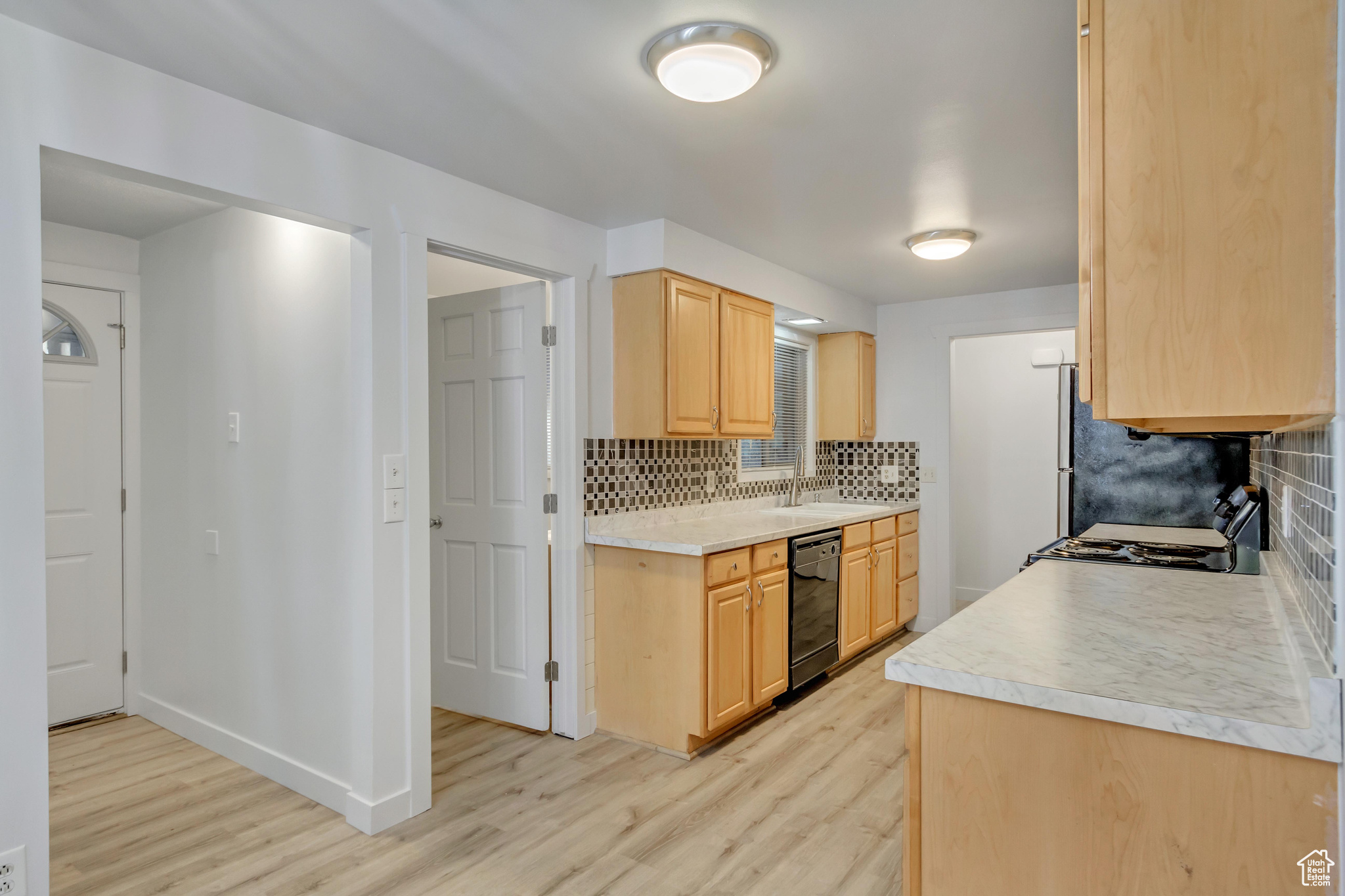 Kitchen with backsplash, black appliances, sink, light brown cabinetry, and light hardwood / wood-style floors