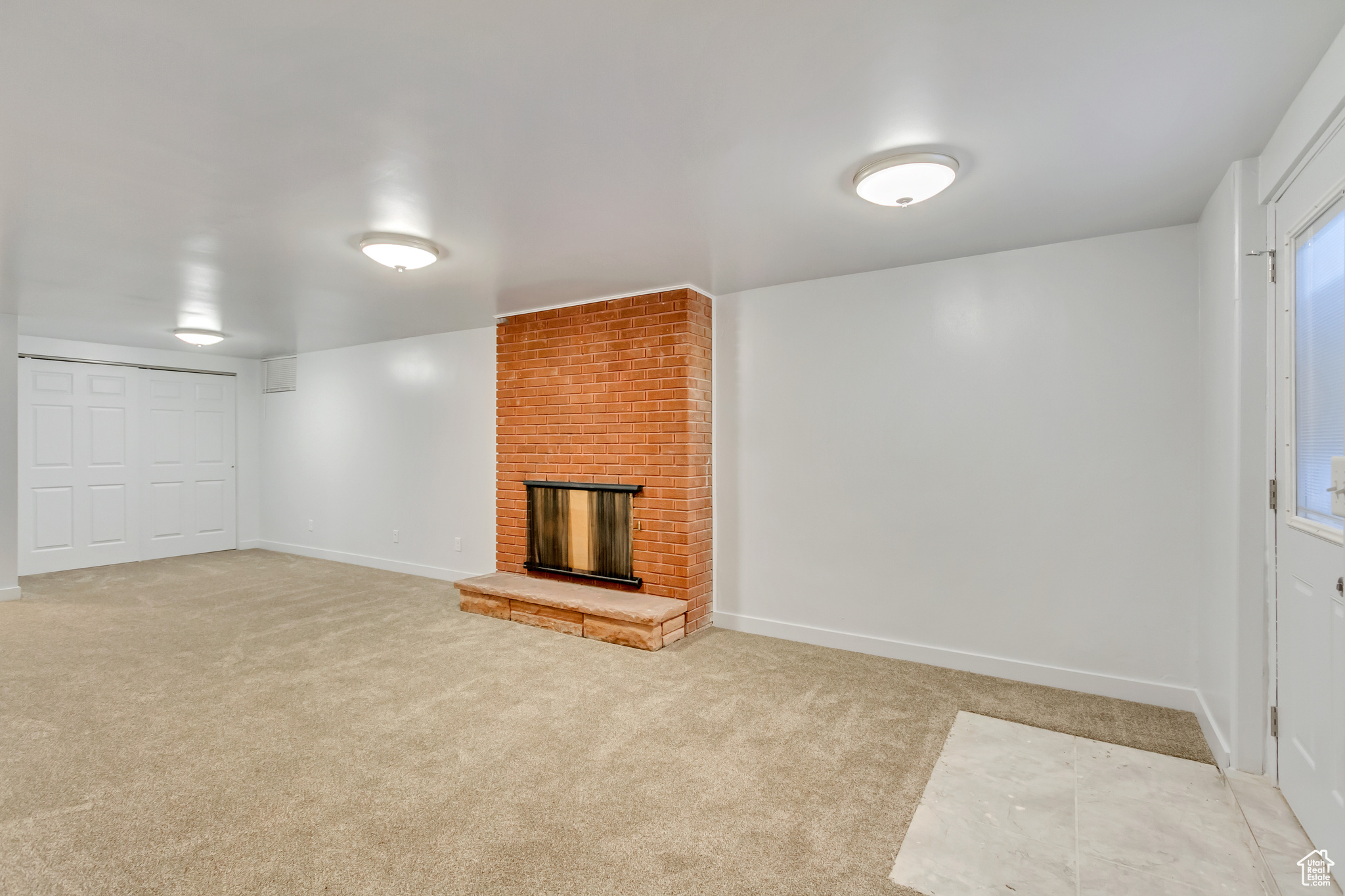 Unfurnished living room featuring light carpet and a brick fireplace