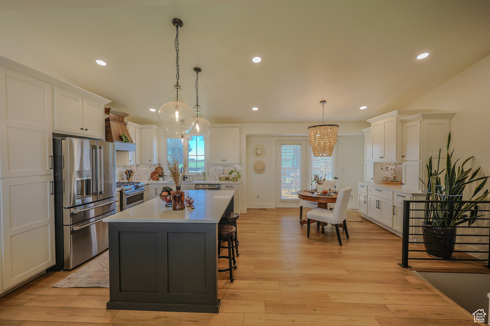 Kitchen with decorative backsplash, stainless steel appliances, a center island, decorative light fixtures, and white cabinetry