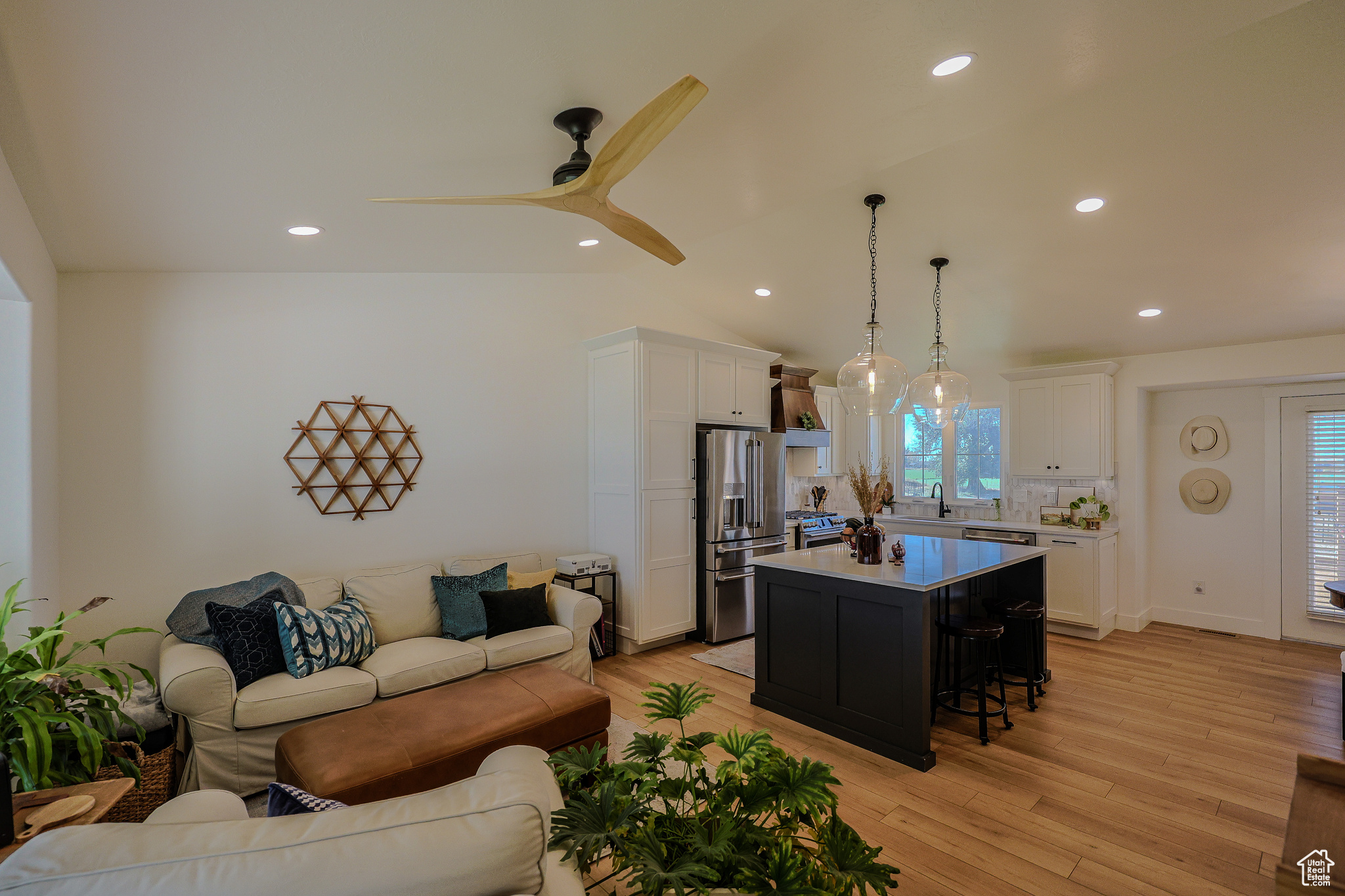 Kitchen featuring appliances with stainless steel finishes, light wood-type flooring, a kitchen island, vaulted ceiling, and pendant lighting