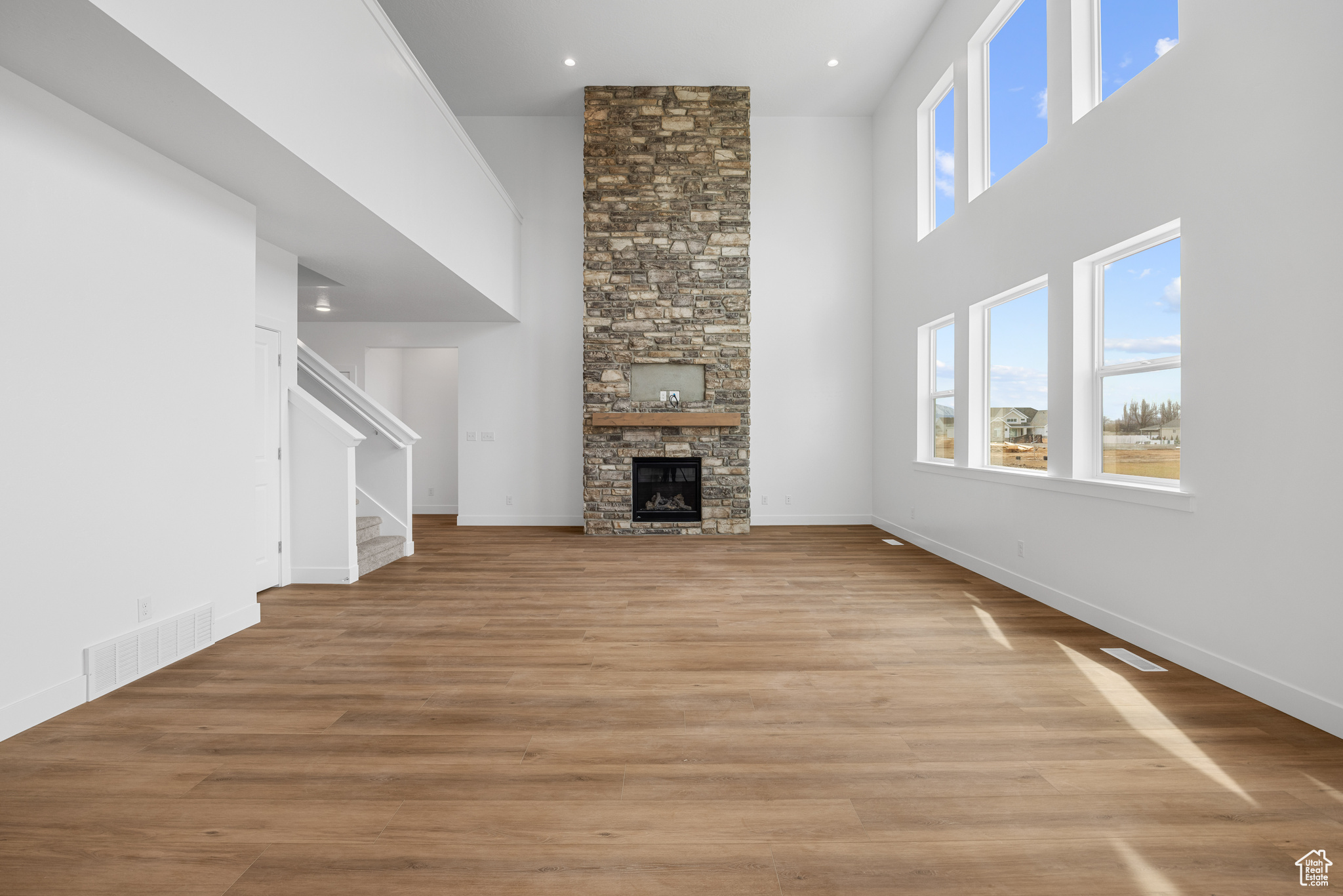 Unfurnished living room with light wood finished floors, stairway, a high ceiling, and visible vents