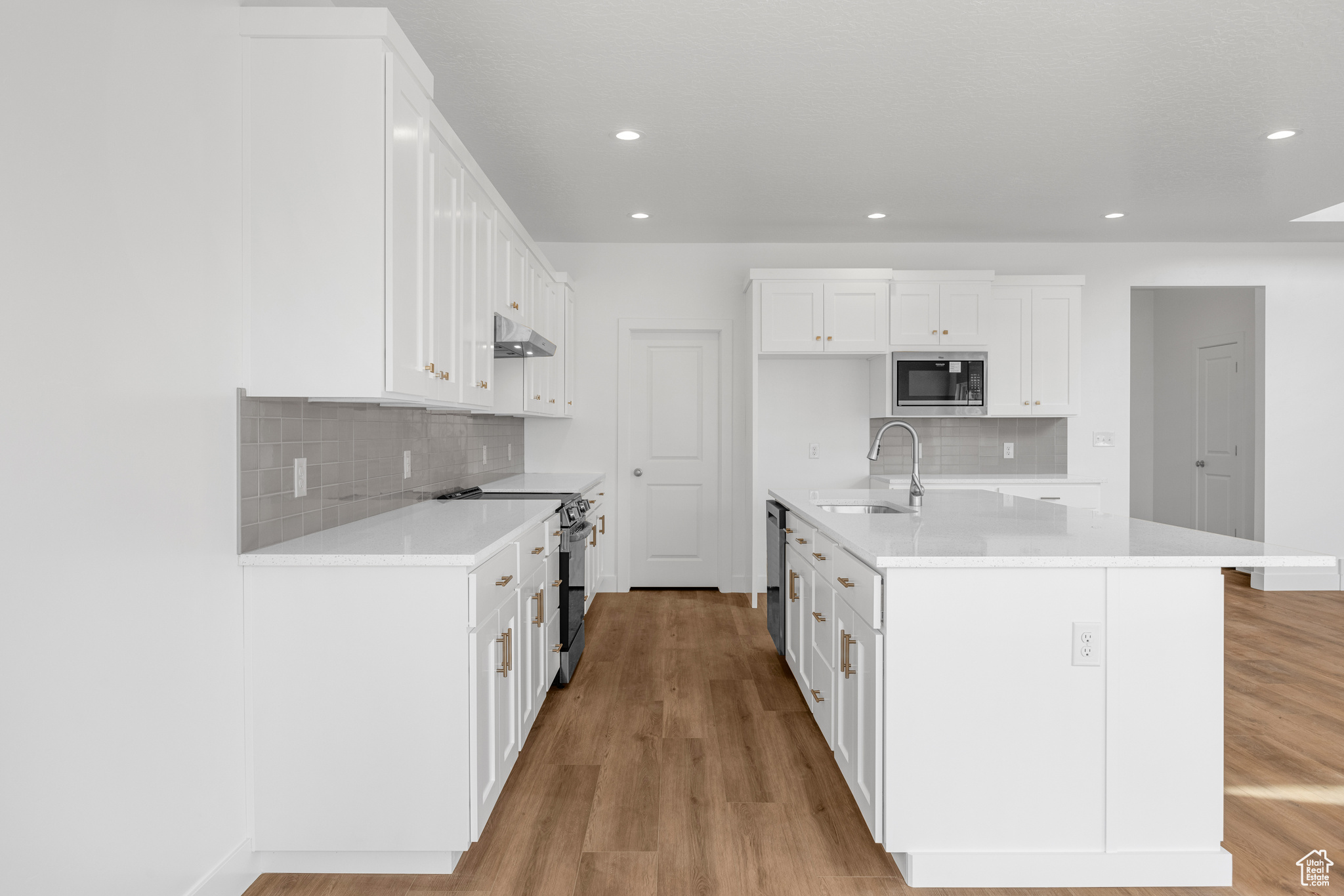 Kitchen featuring light wood-style floors, electric stove, built in microwave, under cabinet range hood, and a sink