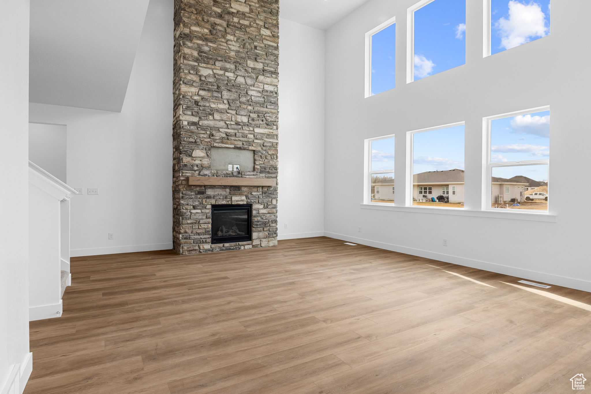 Unfurnished living room featuring a towering ceiling, light wood finished floors, a fireplace, and baseboards