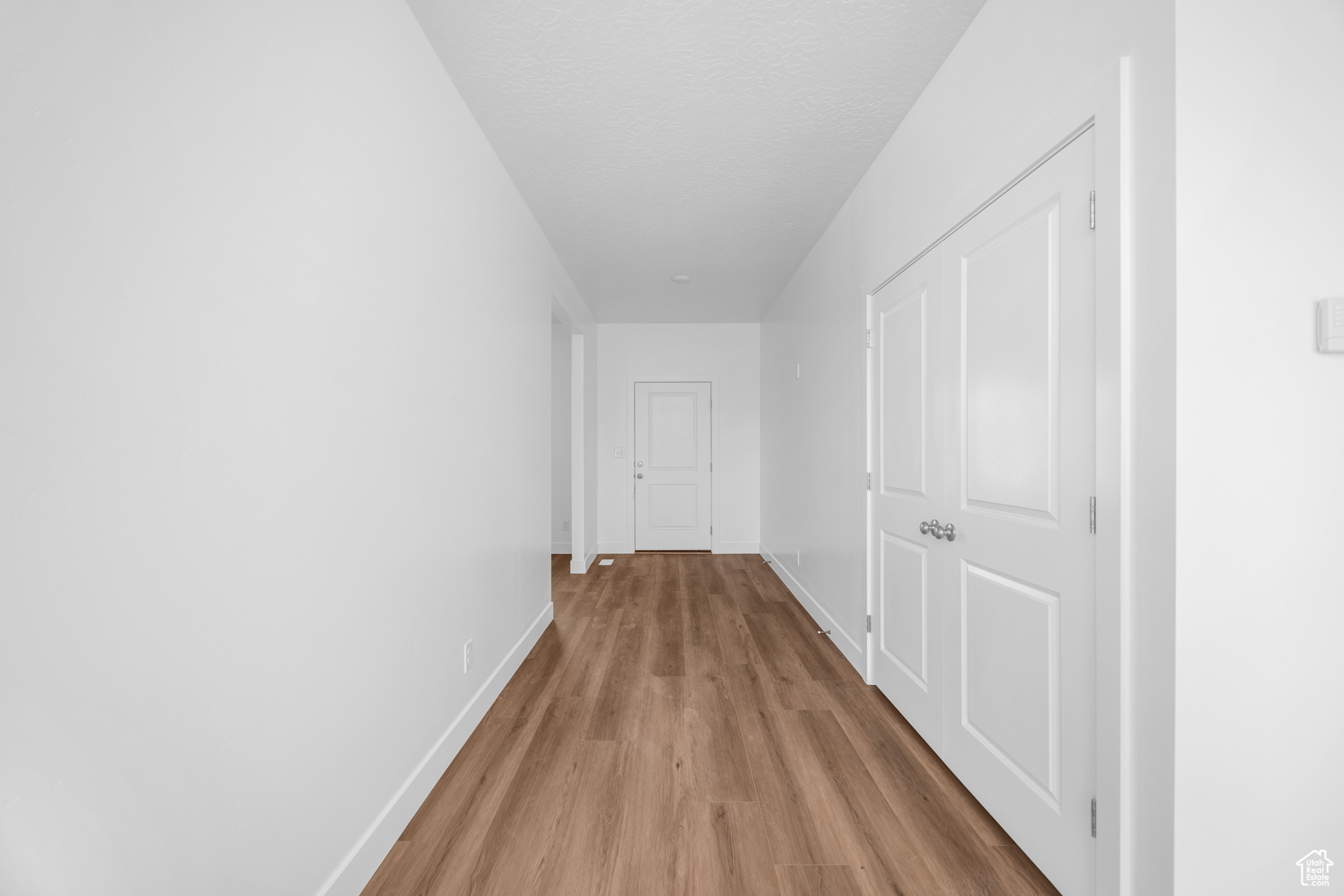 Hallway with light wood finished floors, baseboards, and a textured ceiling