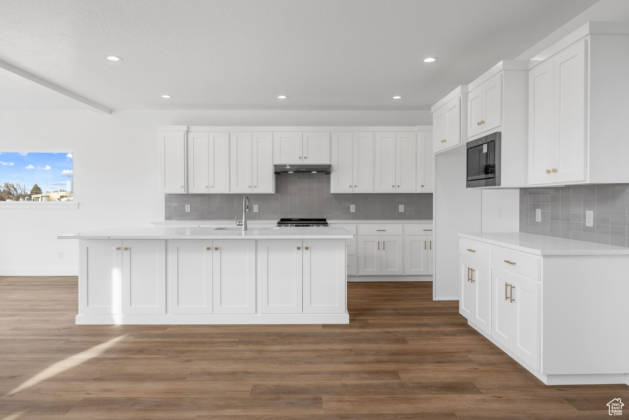 Kitchen featuring under cabinet range hood, white cabinetry, built in microwave, and light countertops