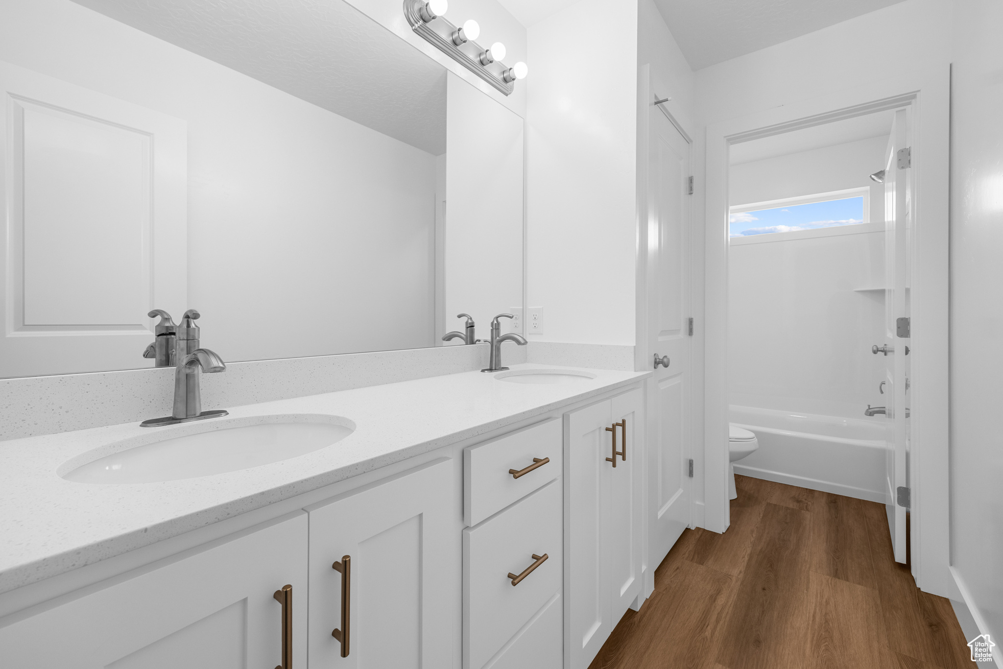 Bathroom with wood finished floors, a sink, toilet, and double vanity