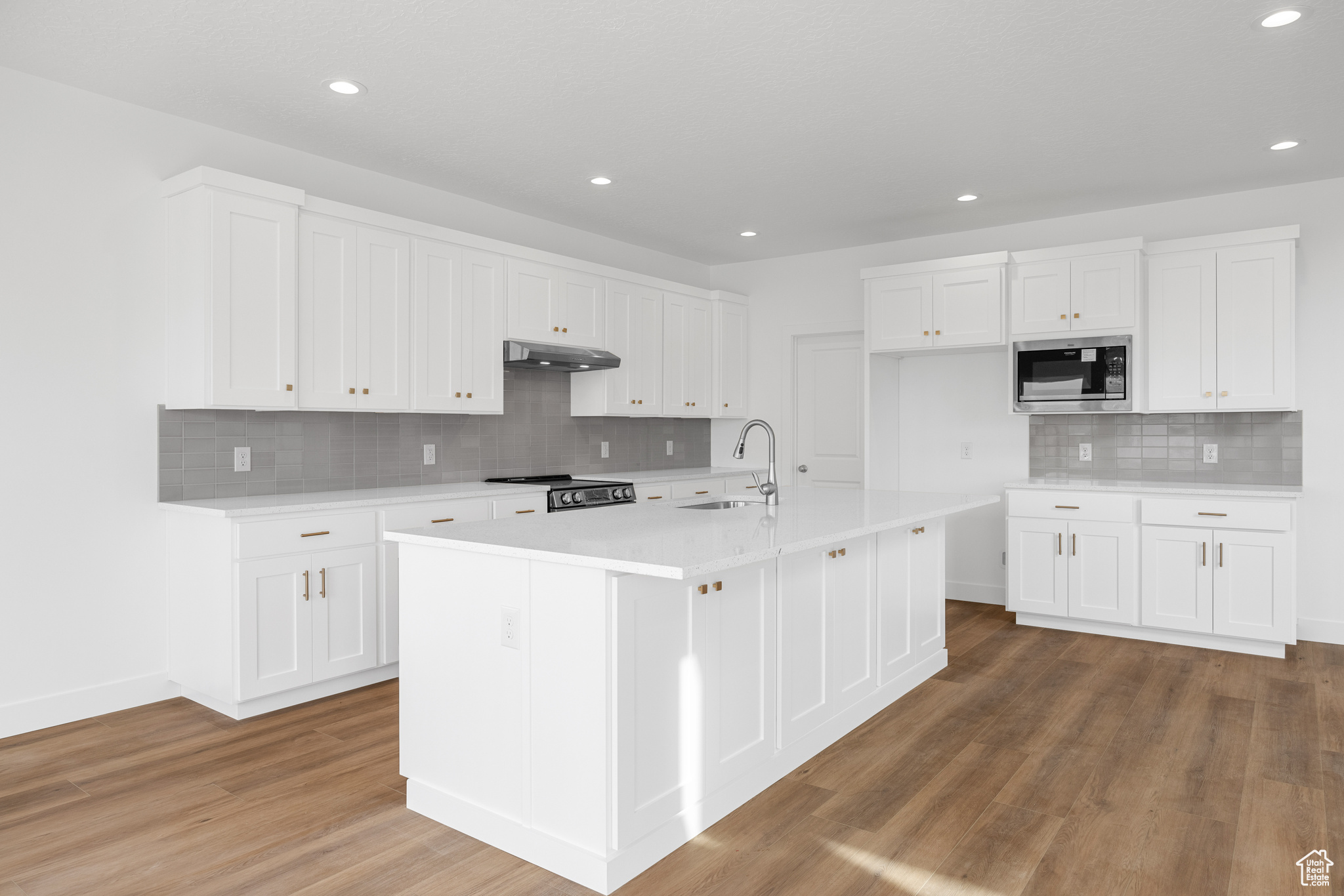 Kitchen featuring light countertops, stainless steel microwave, stove, a sink, and wood finished floors