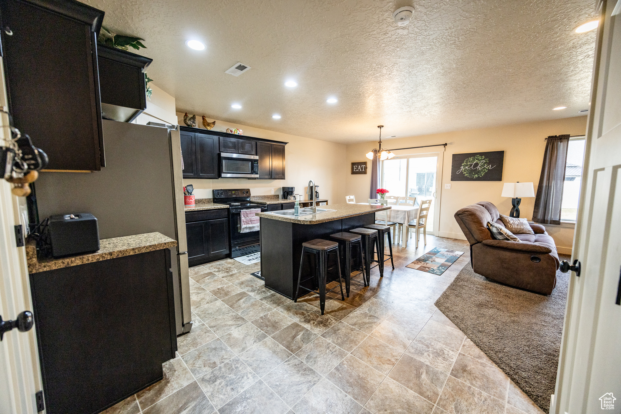 Kitchen with visible vents, stainless steel microwave, a kitchen island with sink, dark cabinetry, and black range with electric cooktop