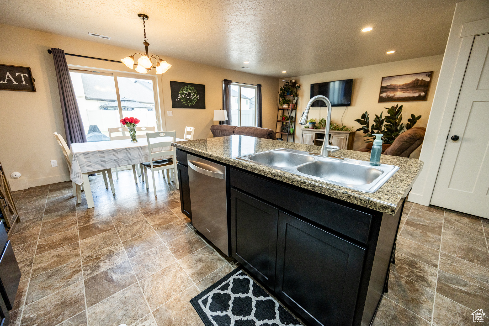 Kitchen featuring decorative light fixtures, a kitchen island with sink, a sink, dark cabinetry, and dishwasher