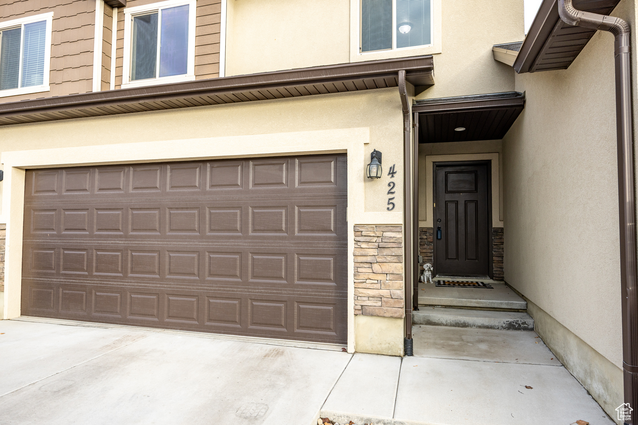 Entrance to property featuring a garage, stone siding, driveway, and stucco siding