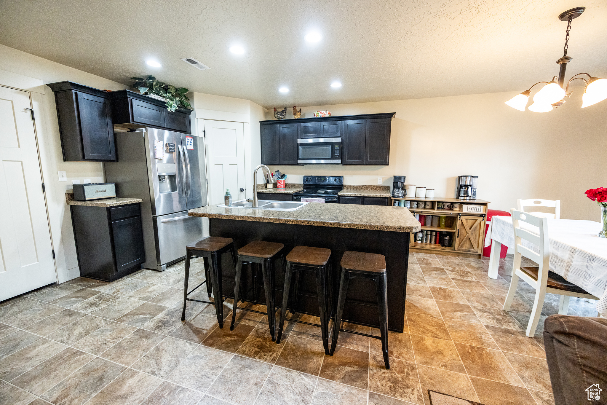 Kitchen with a breakfast bar, stainless steel appliances, a sink, an island with sink, and light stone countertops