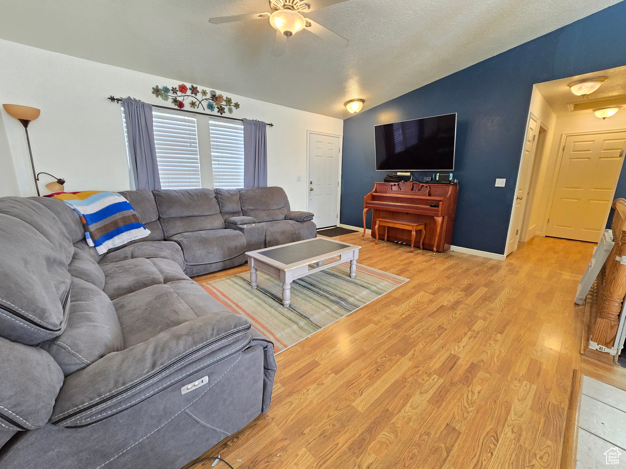 Living room with light hardwood / wood-style floors, a textured ceiling, vaulted ceiling, and ceiling fan