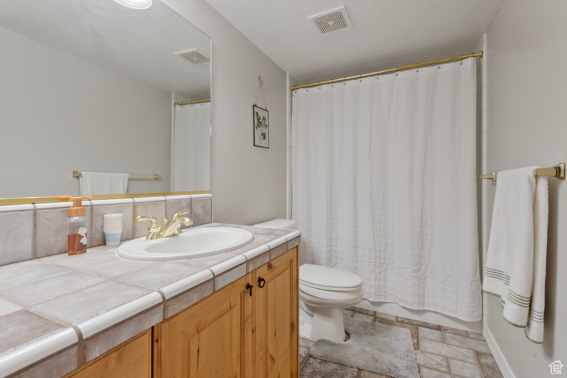 Full bathroom featuring decorative backsplash, shower / tub combo, a textured ceiling, toilet, and vanity