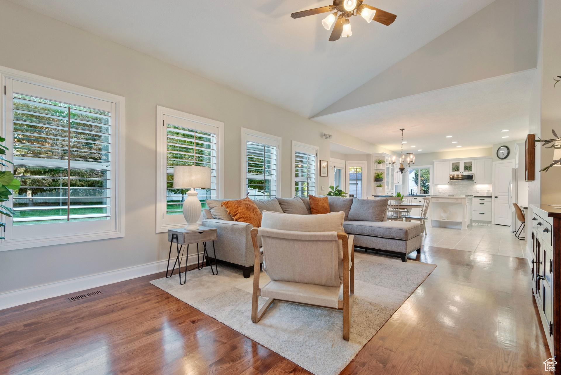 Living room featuring light hardwood / wood-style floors, high vaulted ceiling, ceiling fan with notable chandelier, and plenty of natural light