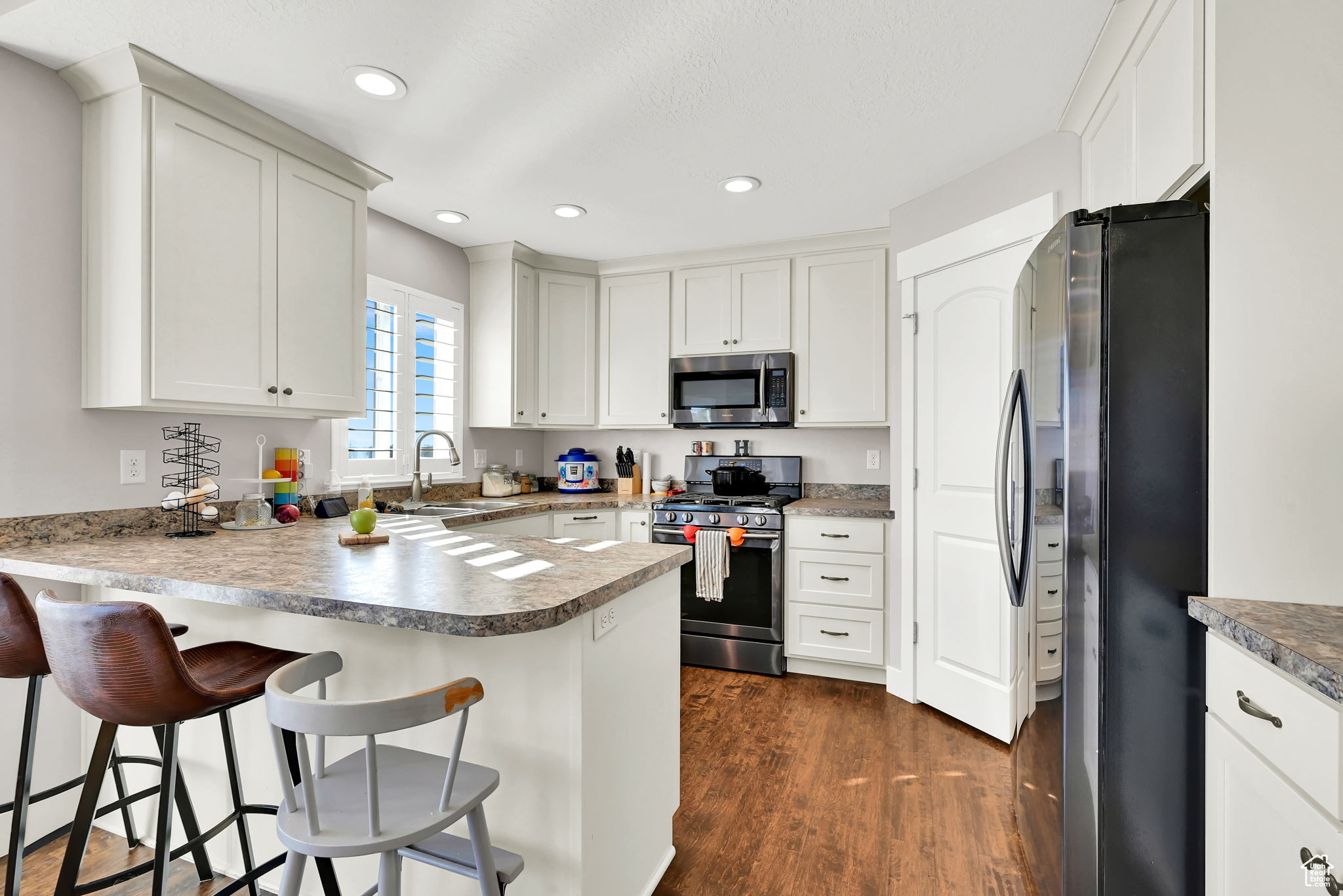 Kitchen with appliances with stainless steel finishes, kitchen peninsula, white cabinets, a breakfast bar area, and dark hardwood / wood-style floors