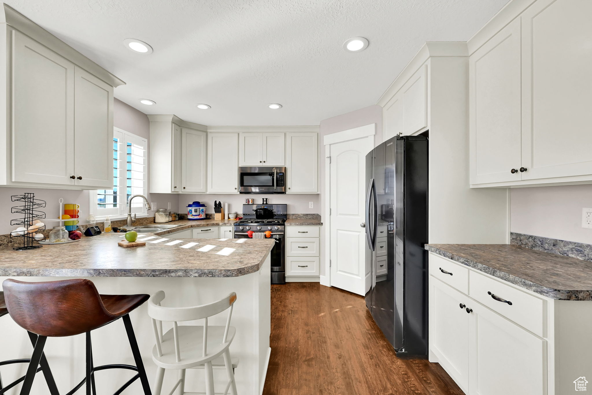 Kitchen featuring appliances with stainless steel finishes, sink, dark hardwood / wood-style flooring, white cabinetry, and a breakfast bar