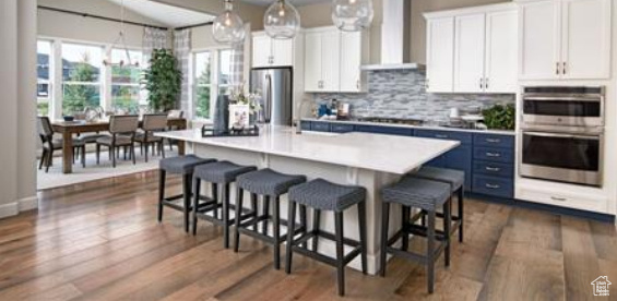 Kitchen with white cabinets, hanging light fixtures, an island with sink, appliances with stainless steel finishes, and range hood. Photos are of a Decker but not the subject property.