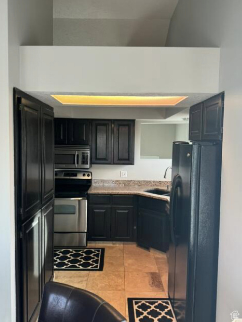 Kitchen with appliances with stainless steel finishes, sink, vaulted ceiling, and light tile patterned floors