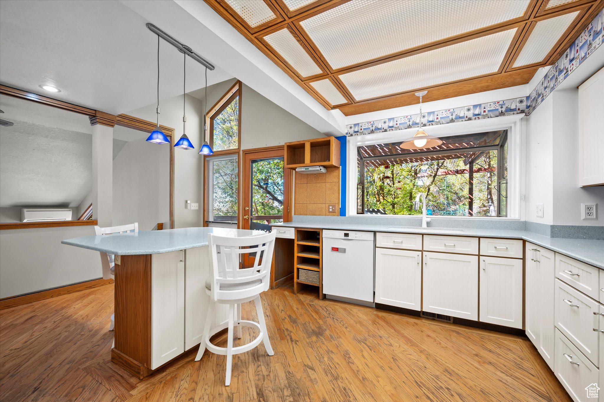 Kitchen featuring white cabinets, a breakfast bar area, light hardwood flooring, dishwasher, and pendant lighting