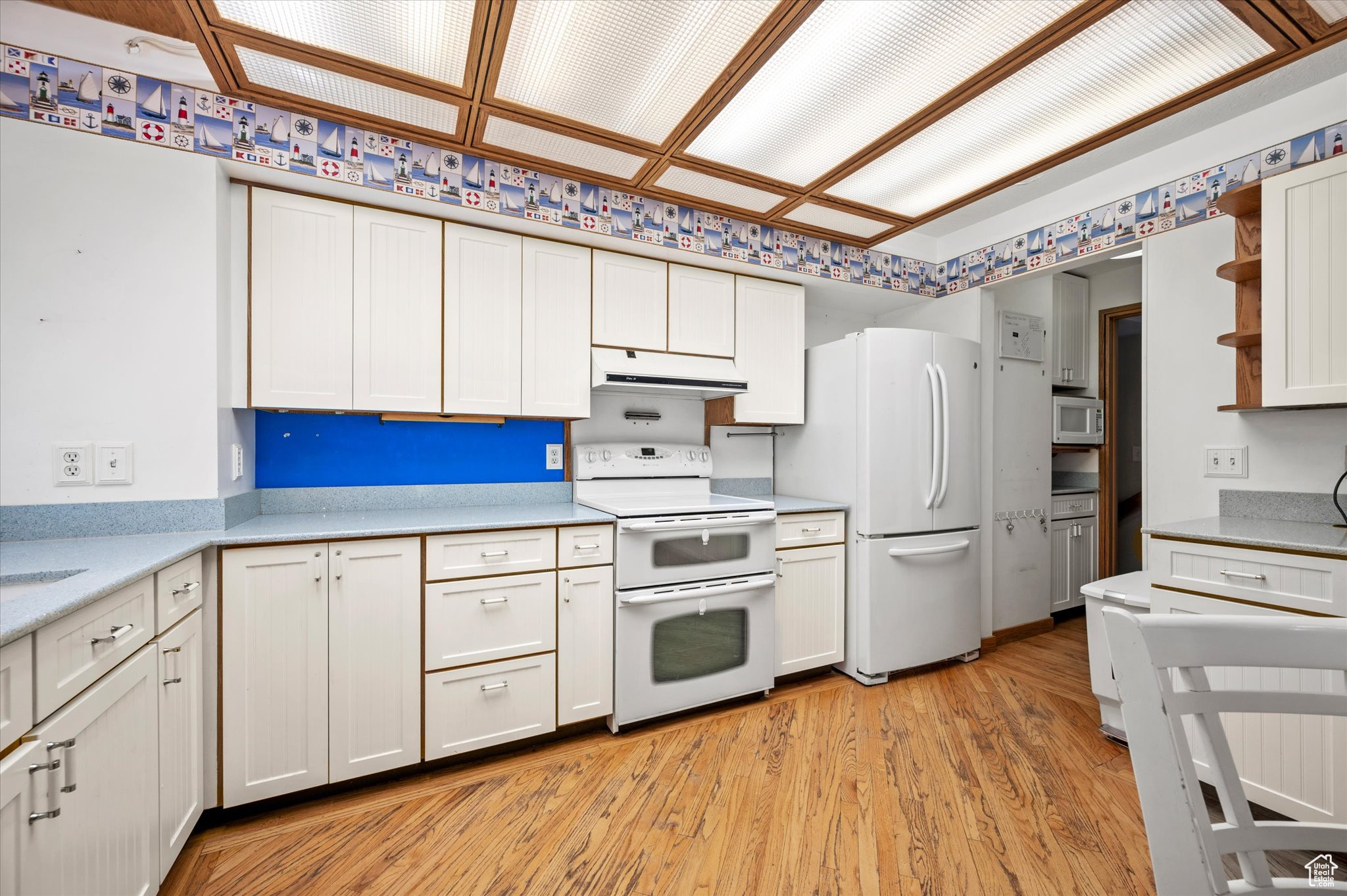 Kitchen with white appliances, light hardwood  flooring, and white cabinets