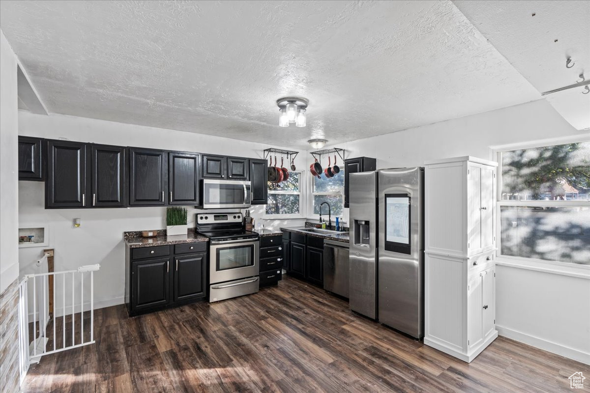 Kitchen with dark wood-type flooring, a textured ceiling, appliances with stainless steel finishes, and sink