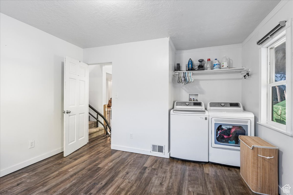 Clothes washing area with dark wood-type flooring, independent washer and dryer, and a textured ceiling