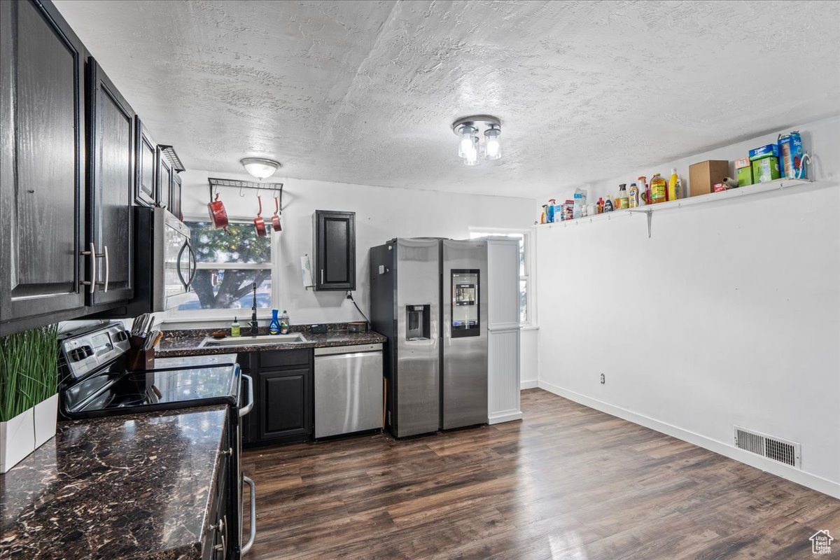 Kitchen featuring dark wood-type flooring, dark stone countertops, appliances with stainless steel finishes, and a textured ceiling